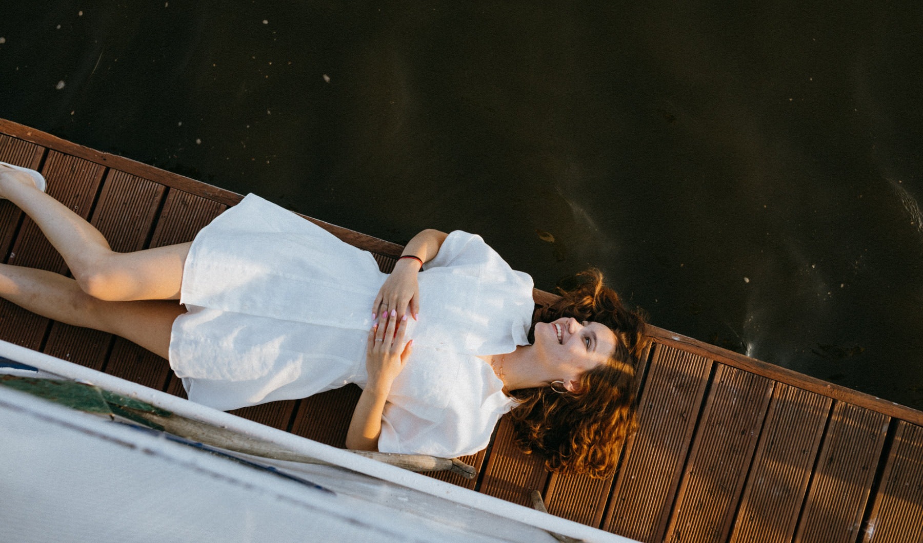 overhead shot of woman lying along pier next to the water